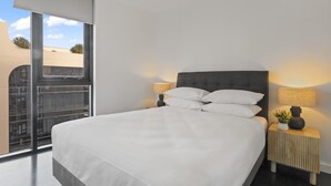 A modern hotel room with a large bed, two bedside tables with lamps, and a view of the city through floor-to-ceiling windows. - Modern 1-bed Apartment Close to Attractions (Melbourne)