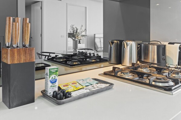 Une cuisine moderne équipée d’une cuisinière à gaz, d’appareils électroménagers en acier inoxydable et d’un plateau contenant des briques de lait et des condiments.