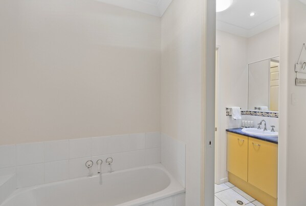 A modern bathroom with a white bathtub, a sink with a blue countertop, and yellow cabinets.