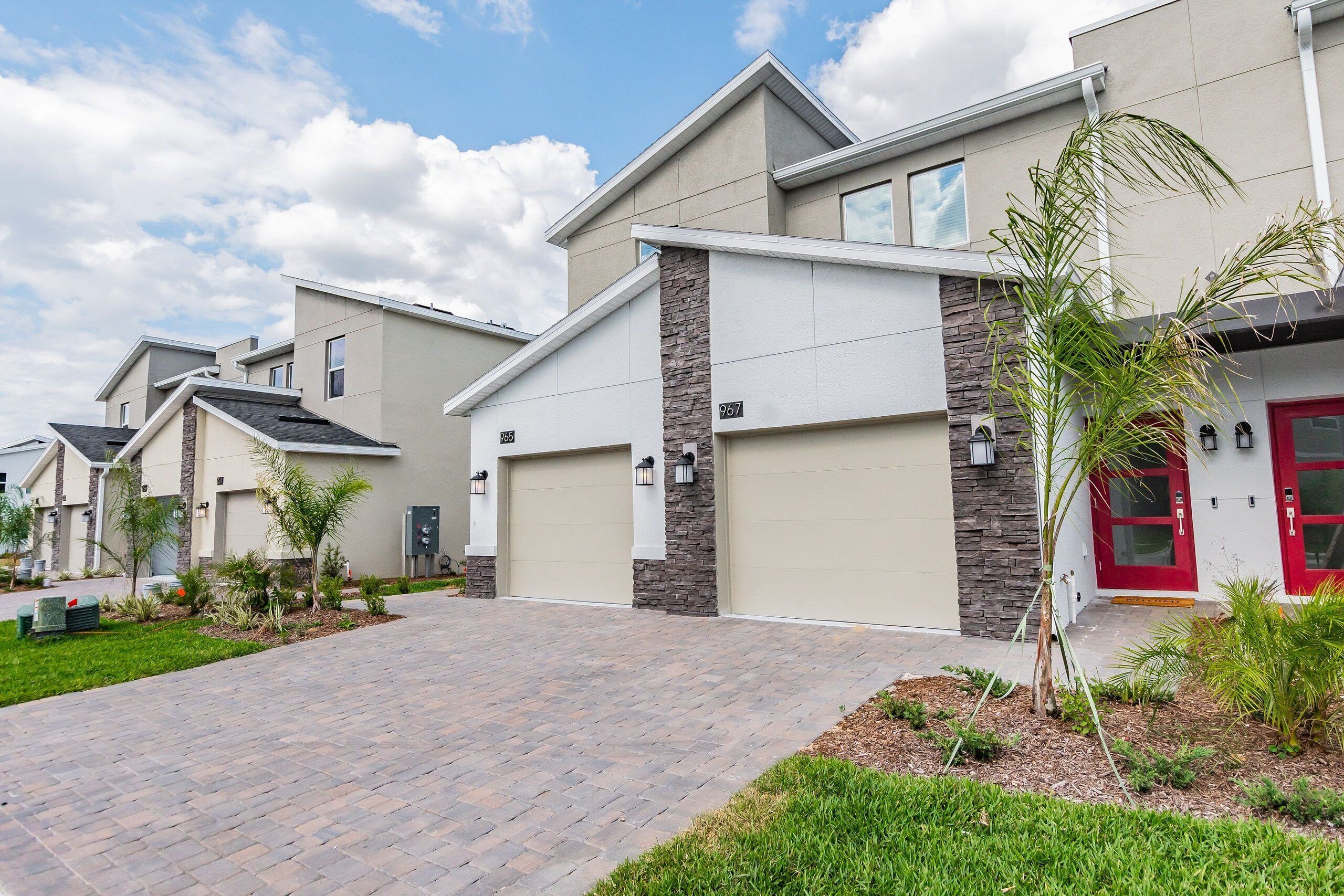 A modern residential building with a paved driveway, stone accents, and a red door.