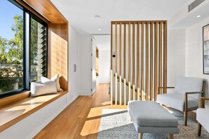 A modern interior with a wooden floor, a sofa, a window seat with cushions, and a wooden partition. - Impeccable 3-bed Home Near the Beach (Sydney)