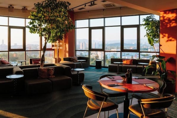 A modern lounge area with large windows, comfortable seating, and a round table. - WN Hotel (Sofia)
