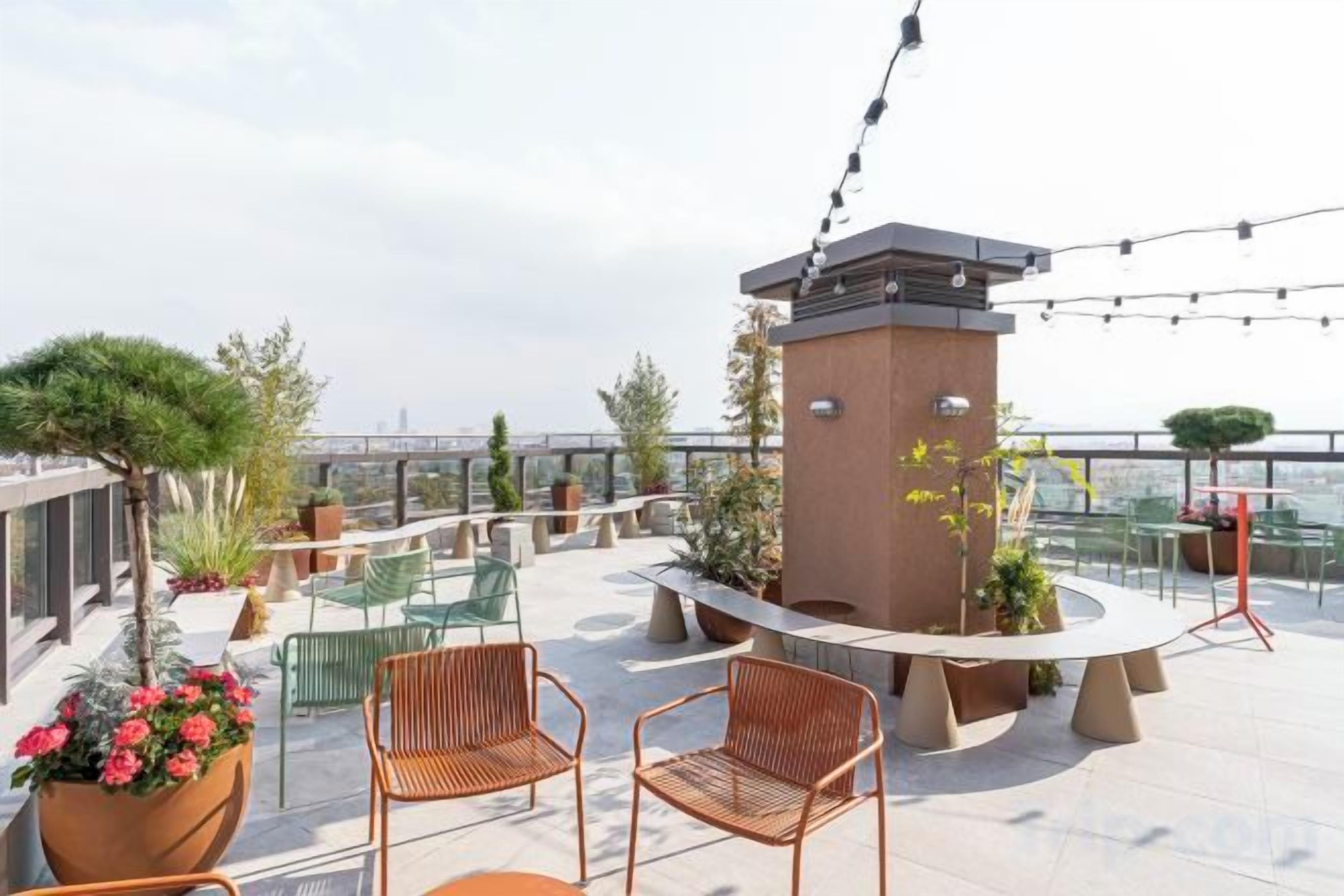 A rooftop terrace with outdoor seating, a central planter, and a view of the cityscape.