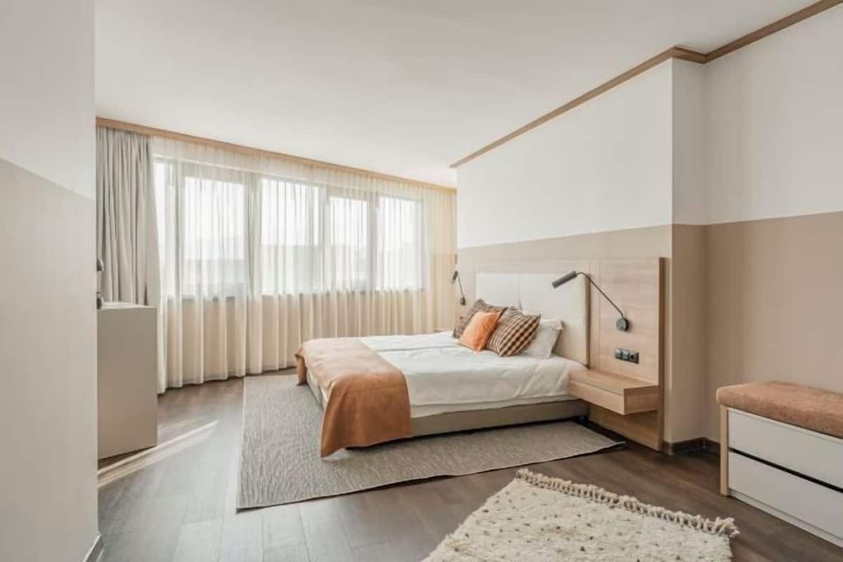 A modern bedroom with a bed, bedside tables, a desk, and a window with curtains.