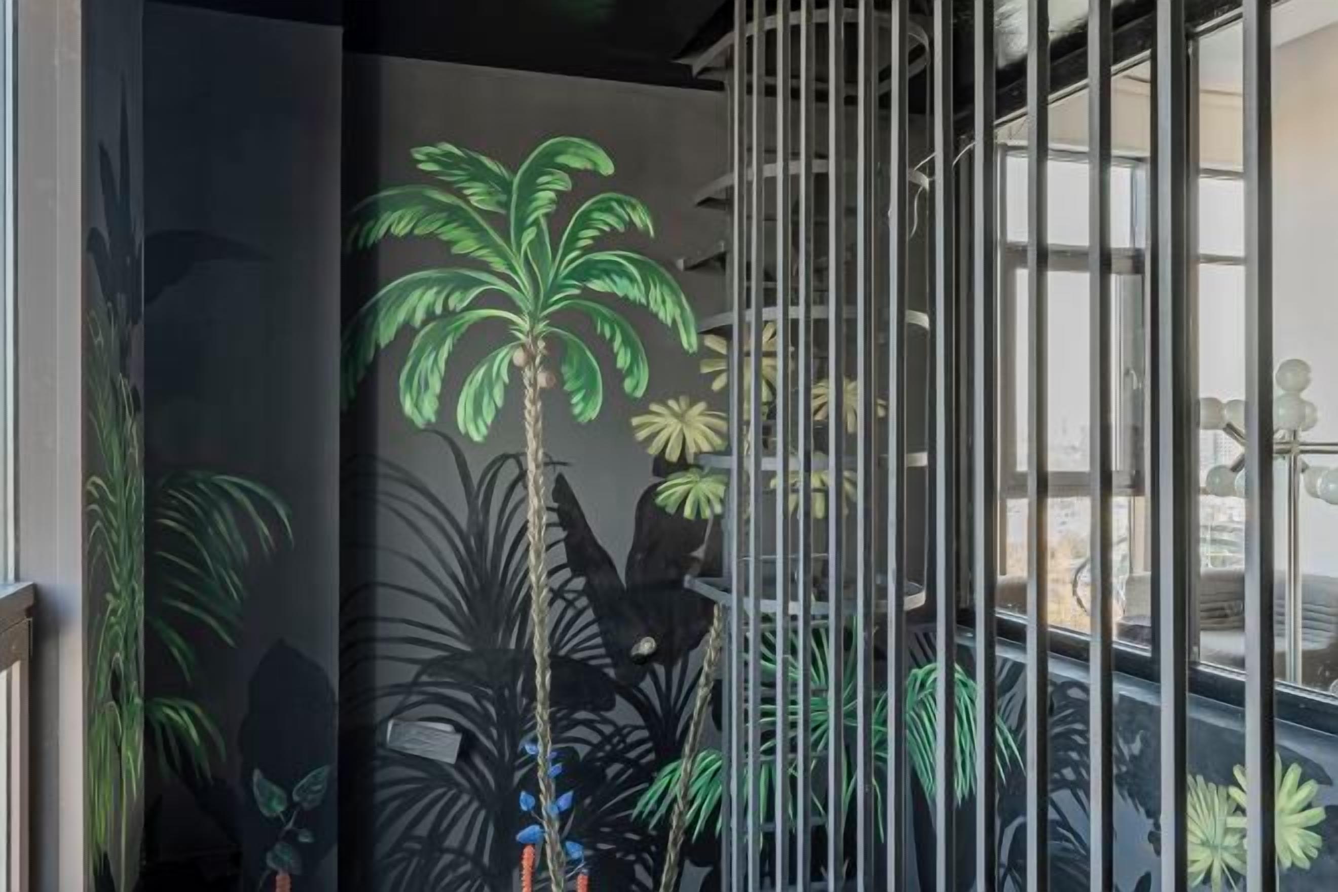 A room with a mural of tropical plants on the wall, a metal gate, and a view of the outside.