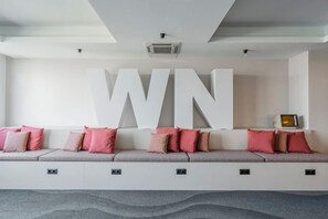 A modern interior with a large white wall-mounted sign reading 'WN,' a white sofa with pink cushions, and a small table with a lamp. - WN Hotel (Sofia)
