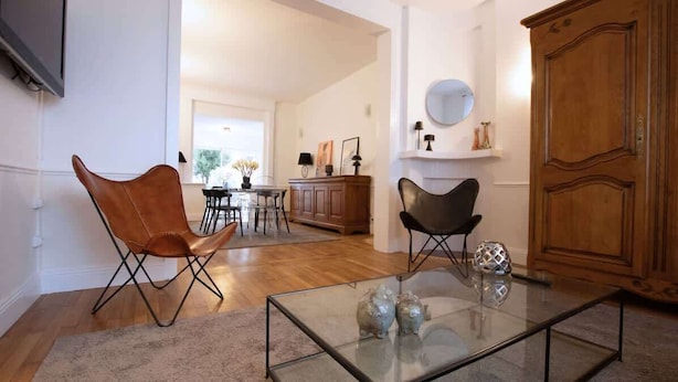 A modern living room with a glass coffee table, leather armchairs, a wooden cabinet, and a dining area in the background. - Villa centrale Douai | 5 ch et terrasse (Douai)