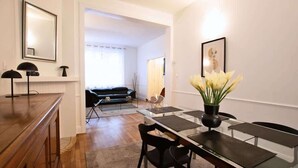 A dining area with a long table, chairs, and a vase of flowers. There is a sofa and a lamp in the background. - Villa centrale Douai | 5 ch et terrasse (Douai)