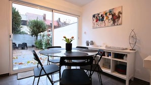 A dining area with a round table and chairs, a vase with flowers, a painting on the wall, and a view of the outside through a sliding door. - Villa centrale Douai | 5 ch et terrasse (Douai)