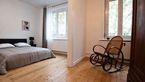 A bedroom with a bed, a rocking chair, a window, and a radiator. - Villa centrale Douai | 5 ch et terrasse (Douai)