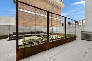 A rooftop terrace with a sectional sofa, a metal fence, and a small garden area. - Sophisticated Inner-city 2-bed With Outdoor Dining (Canberra)