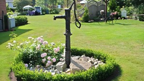 A garden with a water fountain, surrounded by a circular hedge and pink flowers.