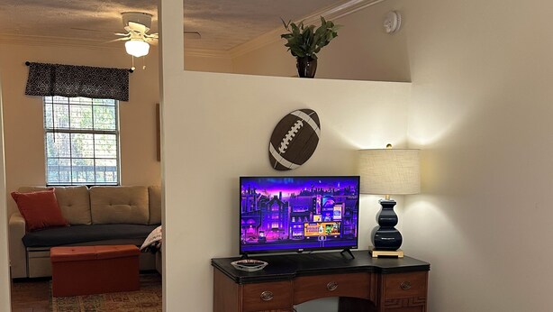 A bedroom with a bed, a desk with a computer, a television, and a window.
