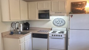 A compact kitchen with white cabinets, a microwave, a stove, and a refrigerator.