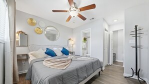 A bedroom with a bed, ceiling fan, wall decor, and a coat rack.