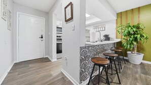 A modern kitchen with a bar area, wooden stools, and a potted plant.