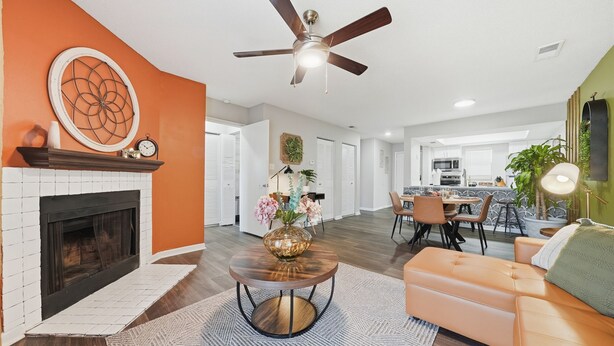 A spacious living area with a fireplace, a ceiling fan, and a dining area in the background.