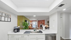 A modern kitchen with white cabinetry, a coffee station, and a view into the dining area.