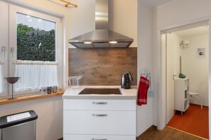A modern kitchen with a built-in stove, a stainless steel range hood, and a window with a view of greenery. - Apartment 'Ferienwohnung, 60qm' with Shared Terrace, Shared Garden and Wi-Fi (Olsberg)
