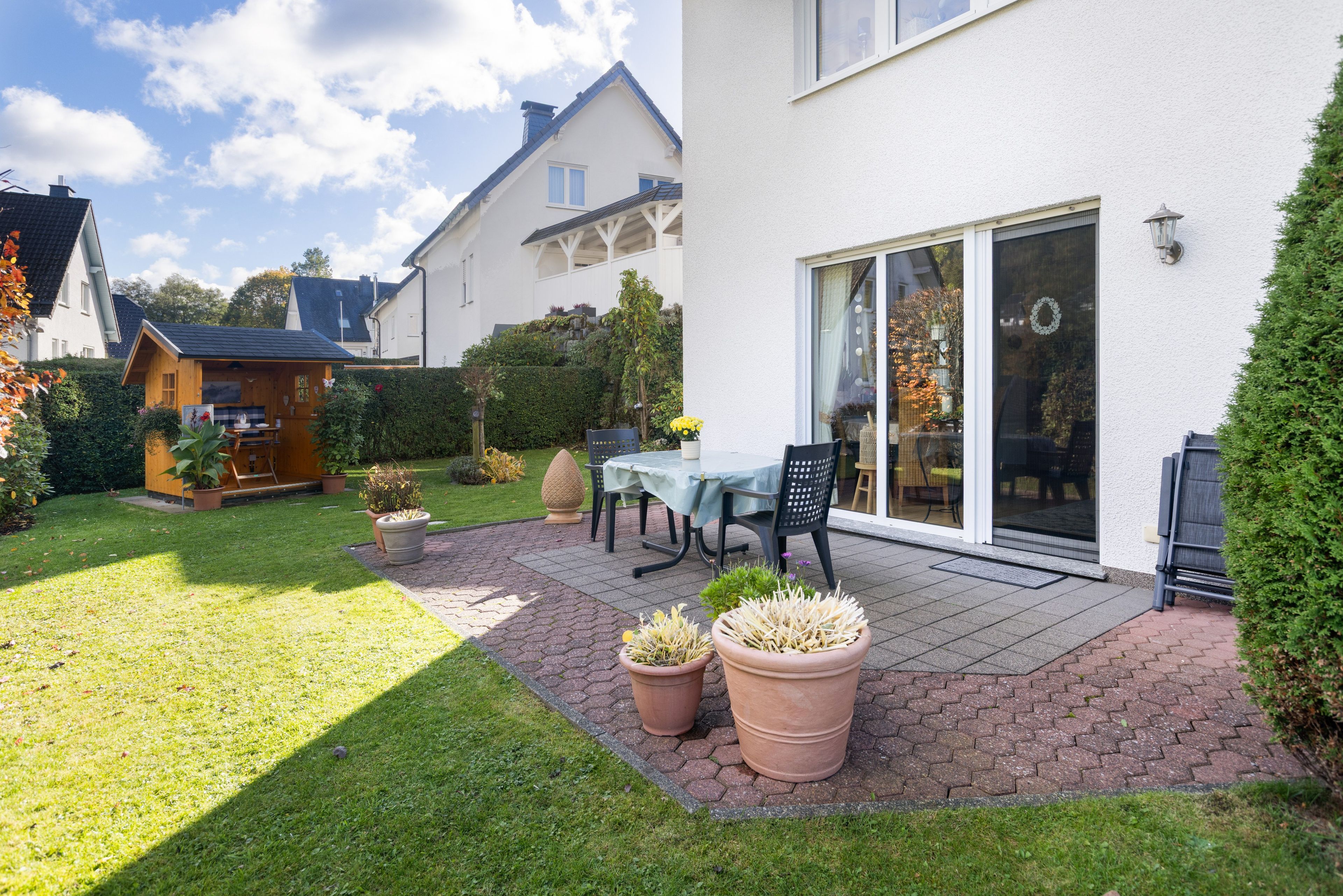 A patio with a table and chairs, surrounded by potted plants and a grassy lawn.