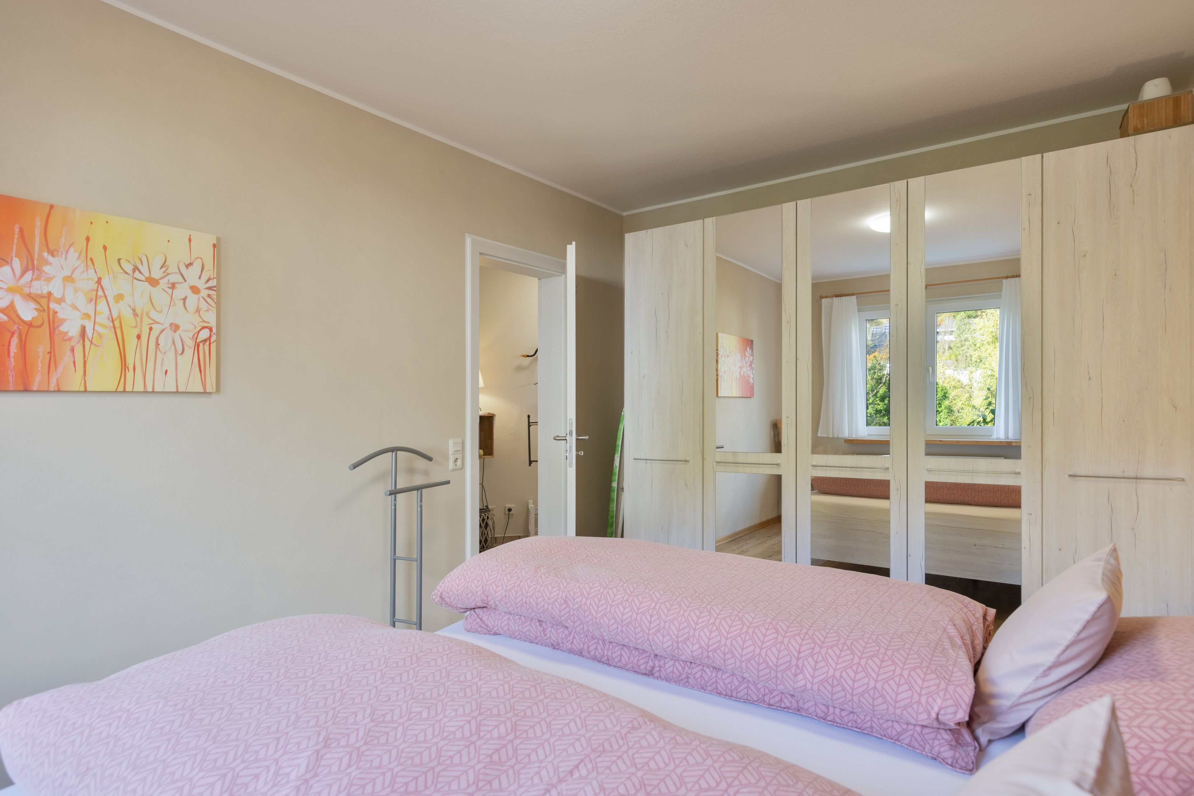 A bedroom with two beds, a wardrobe, and a painting on the wall.