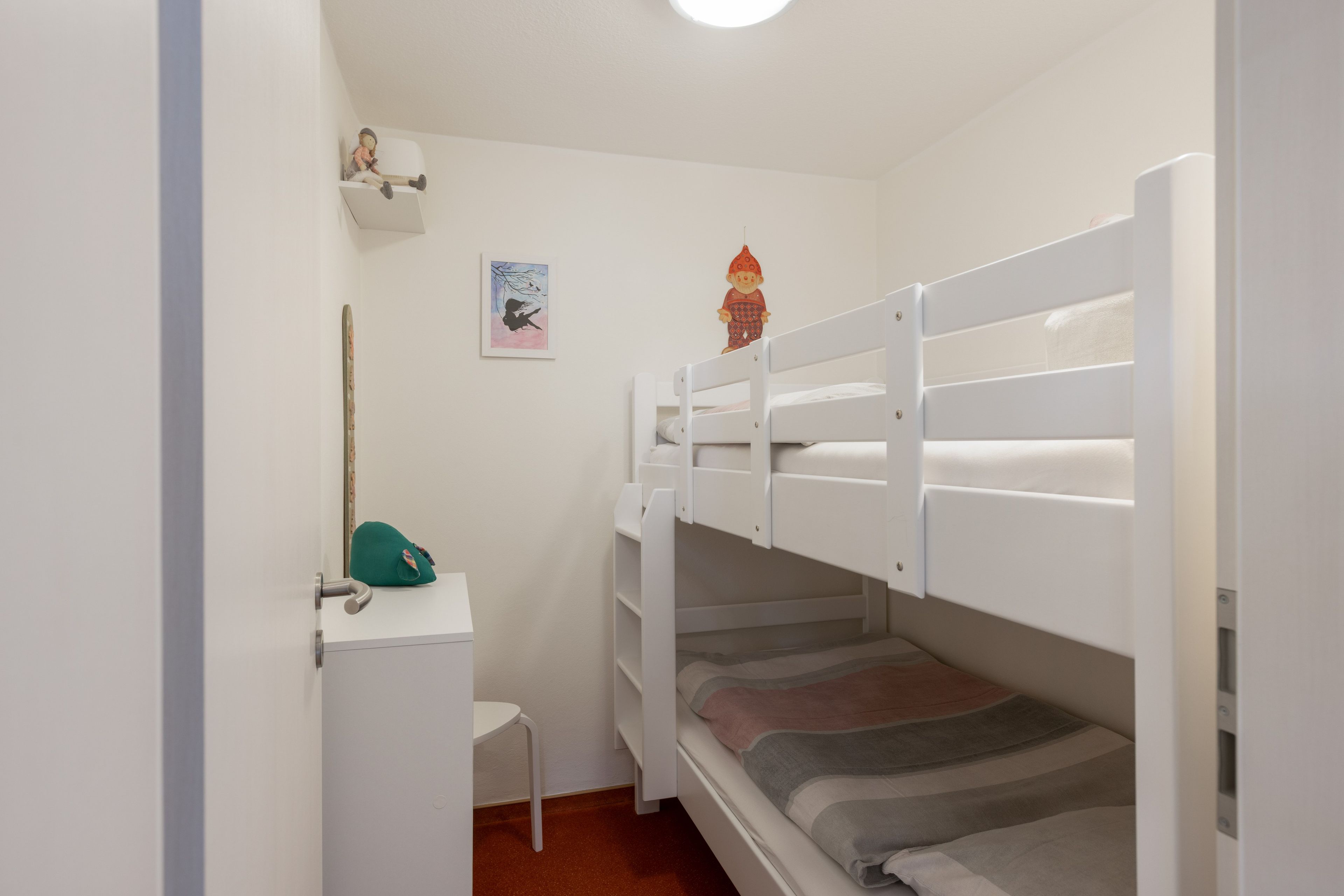 A bunk bed room with a desk and chair, a small table, and a wall-mounted shelf.