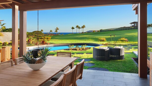 Un patio exterior con una mesa y sillas de madera, un cuenco de fruta y vistas a un campo de golf y al océano.