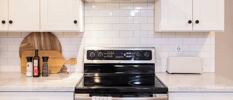 A kitchen with white cabinets, a stainless steel stove, a toaster, and a wooden cutting board with bottles of olive oil and salt.