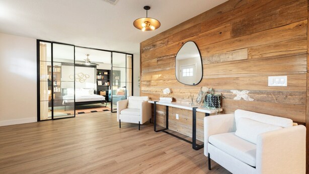 A modern bedroom with a wooden accent wall, a large mirror, a bedside table, and a white sofa. - Arcadia Oasis | Heated Pool & Near Old Town (Phoenix)