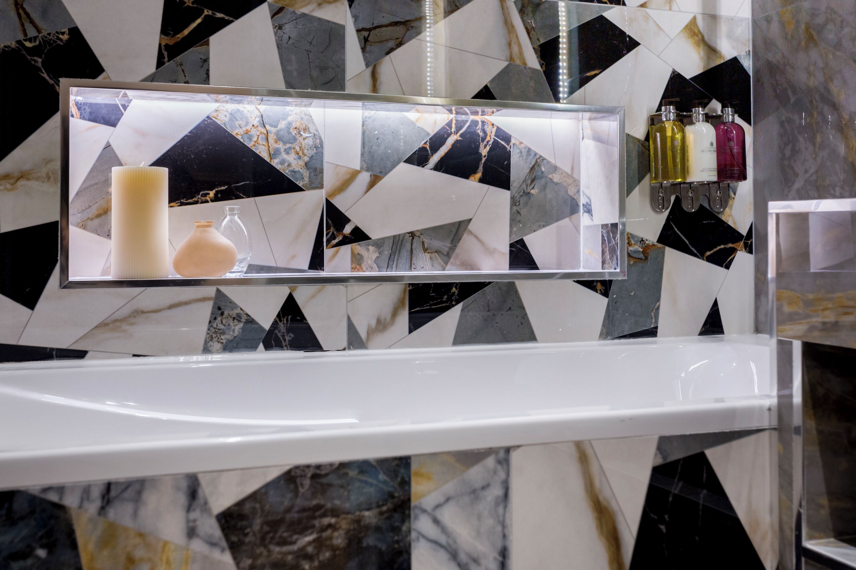 Une salle de bain avec une baignoire blanche, un miroir avec des articles de toilette et un mur décoré d’un motif marbré.