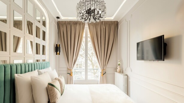 A bedroom with a large bed, a TV mounted on the wall, and a window with curtains. - Merveil Signature Suite - Kleber (Paris)