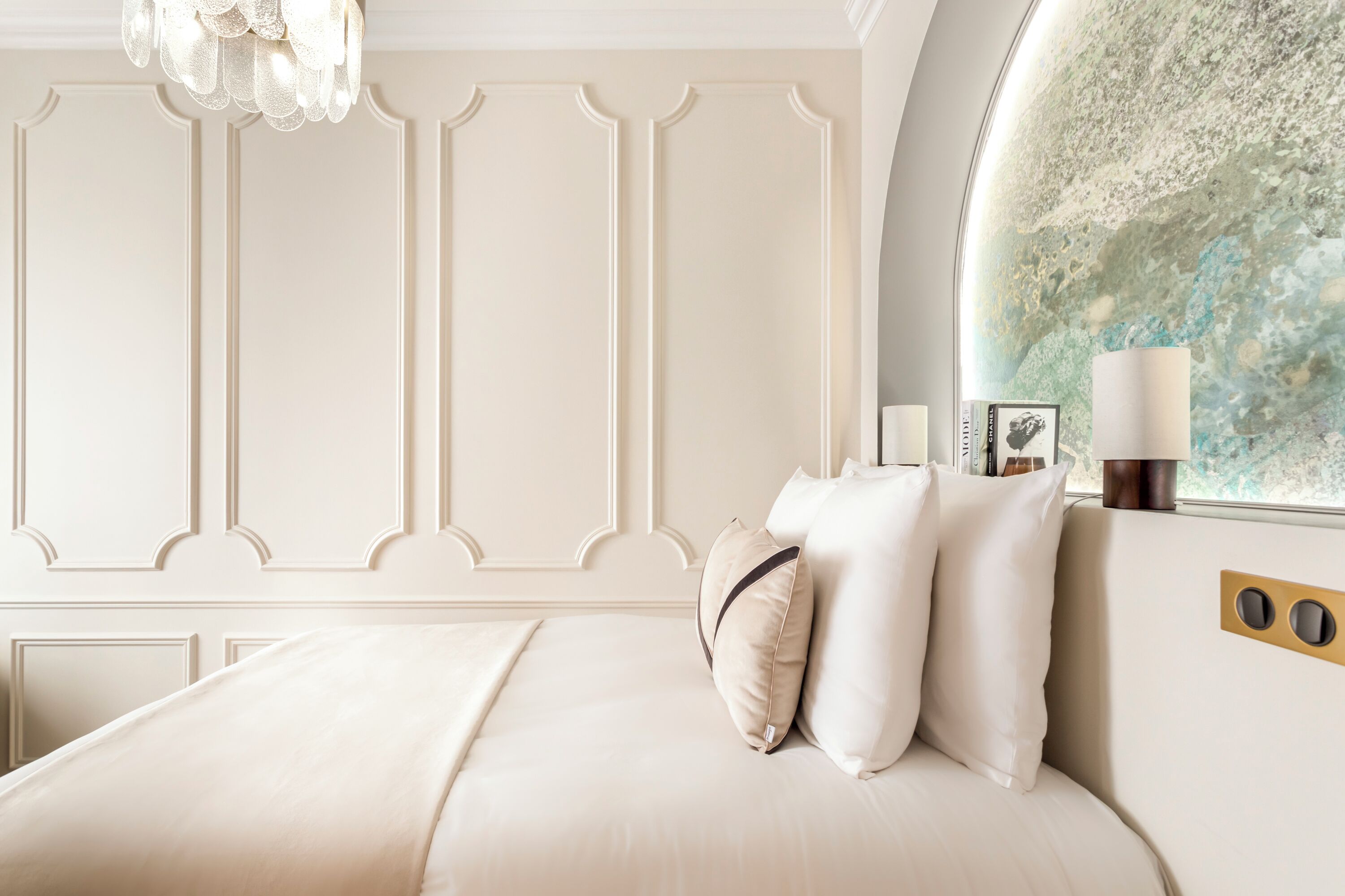 Habitación de hotel con una cama grande, una araña y un panel decorativo en la pared.