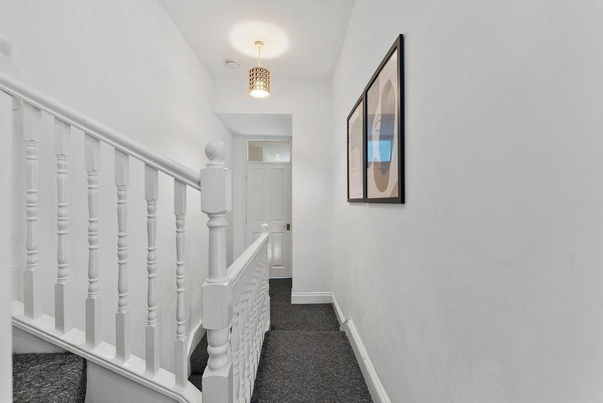 A staircase with white balusters leading to a landing, a framed picture on the wall, and a ceiling light fixture.