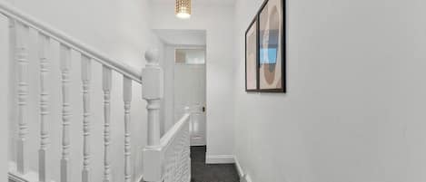 A staircase with white balusters leading to a landing, a framed picture on the wall, and a ceiling light fixture.