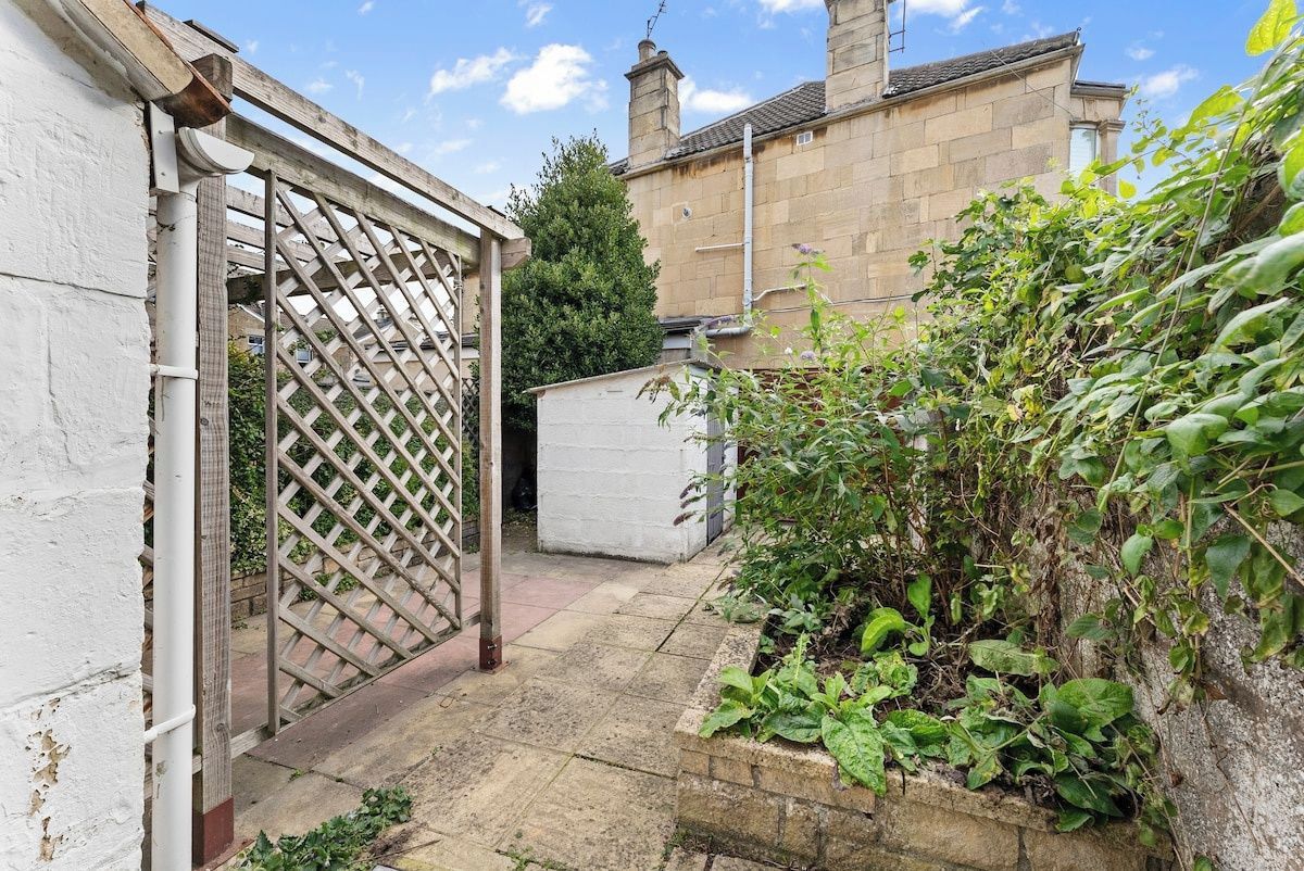 A garden with a wooden gate, a white shed, and a stone wall.