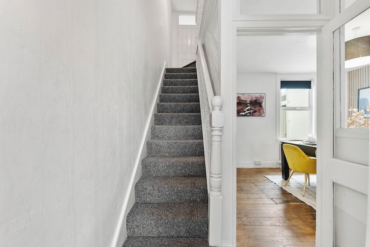 Escadaria com corrimão branco que leva a um quarto com piso de madeira e uma cadeira amarela.