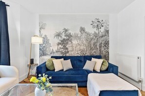 Ein Wohnzimmer mit einem blauen Sofa, einem Couchtisch mit Blumenvase und einer großen Wandmalerei.