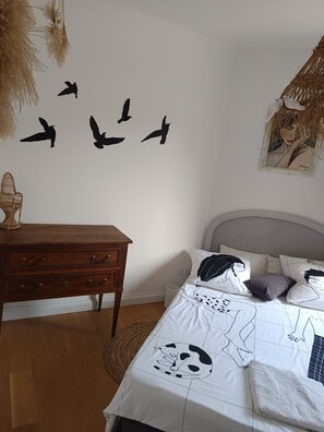 A bedroom with a bed, a dresser, a wall with bird silhouettes, and a hanging decoration.