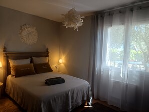 A bedroom with a bed, bedside lamps, a hanging light fixture, and a window with curtains. - Dream Vacation (Verfeil)