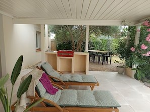 A covered outdoor seating area with two lounge chairs, a small table, and a red appliance.