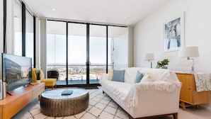 Una sala de estar moderna con un ventanal grande, un sofá, una mesa de centro y un televisor sobre un mueble de madera.