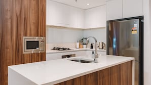 Una cocina moderna con armarios blancos, un refrigerador de acero inoxidable, un microondas integrado y una estufa a gas.