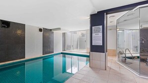 Une piscine avec un mur en verre, un panneau indiquant les règles et un sol carrelé.