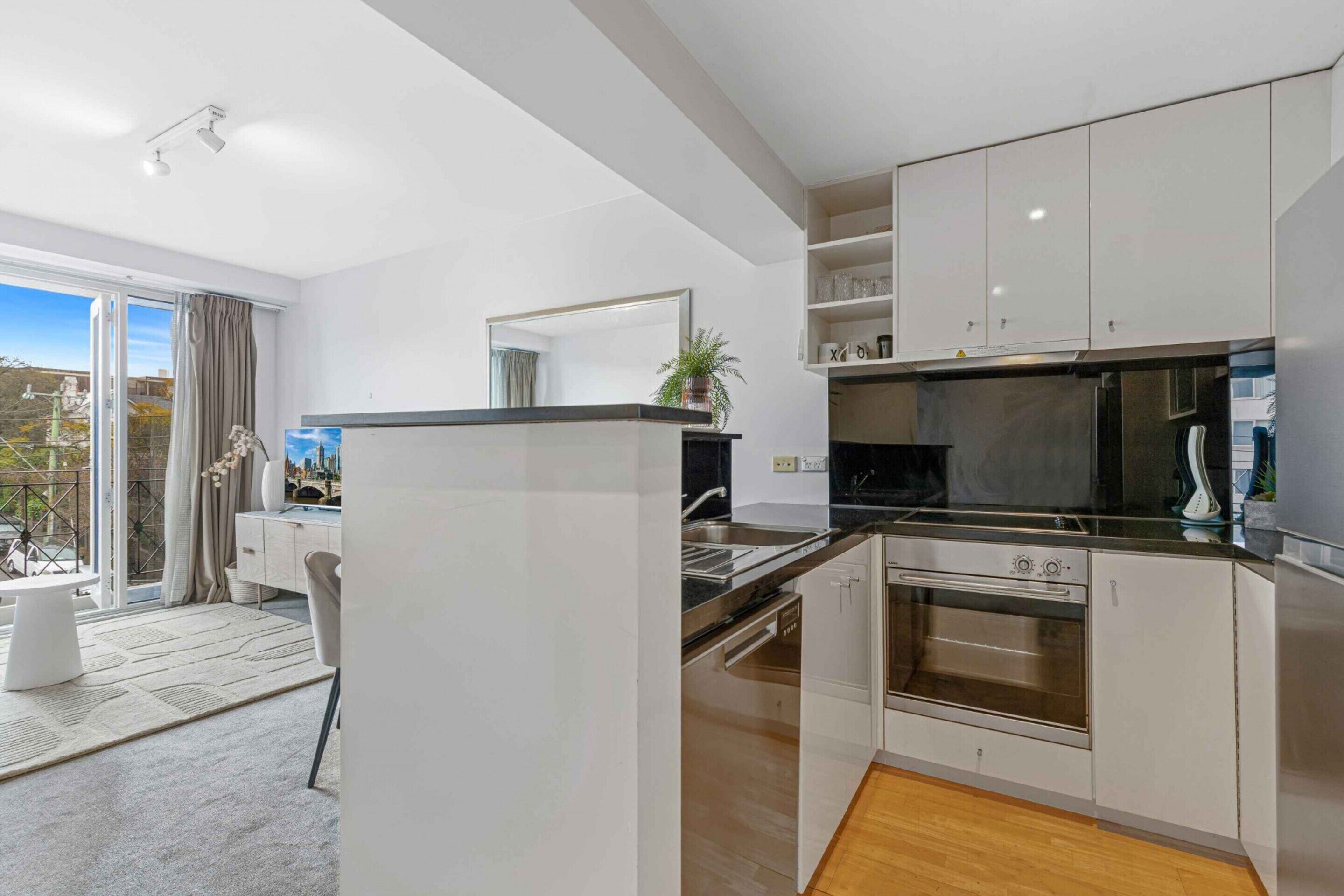 A modern kitchen with white cabinetry, a built-in oven, and a large window overlooking a cityscape.