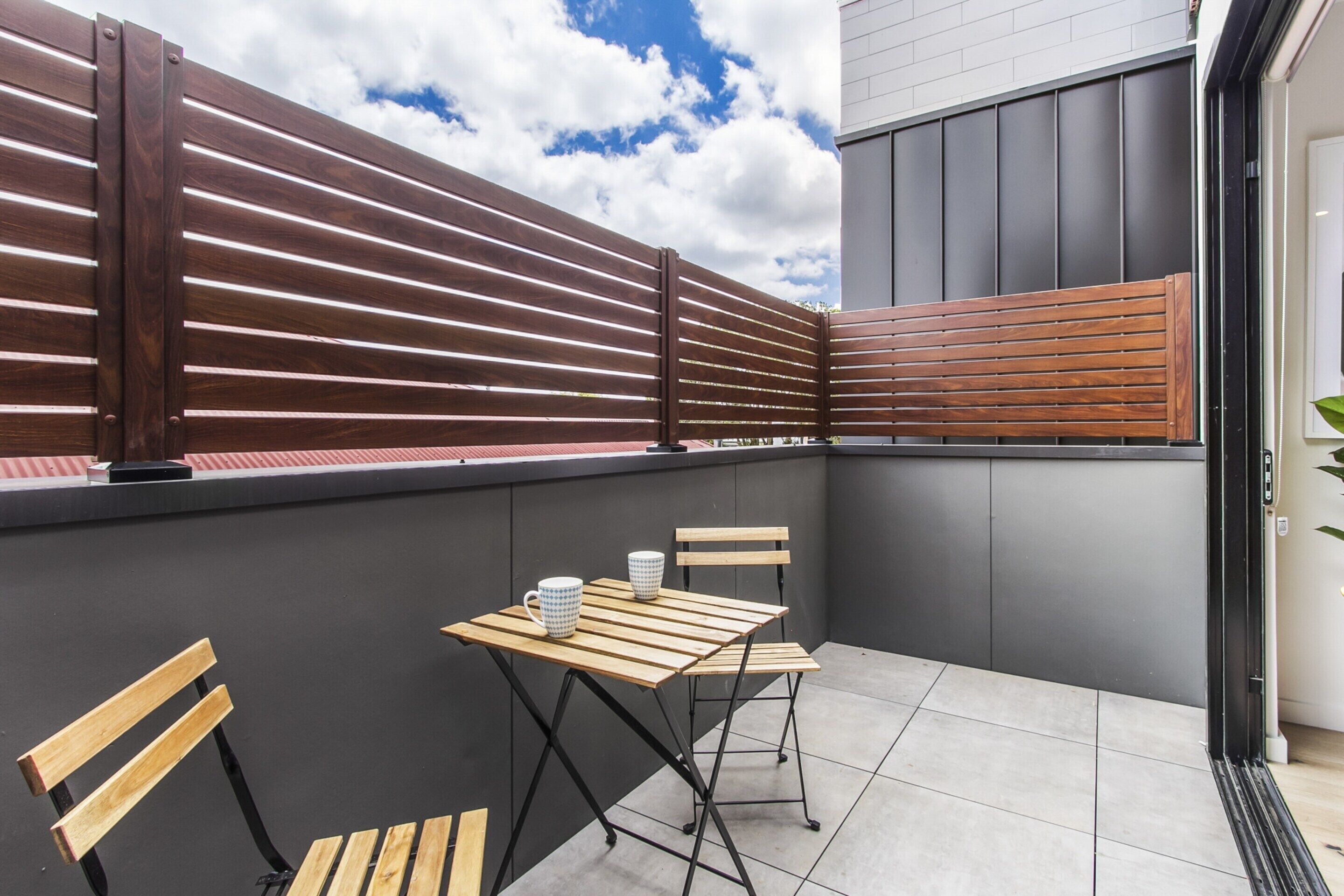 Ein Balkon mit Holztisch und -stühlen, einem Holzzaun und einer grauen Wand.