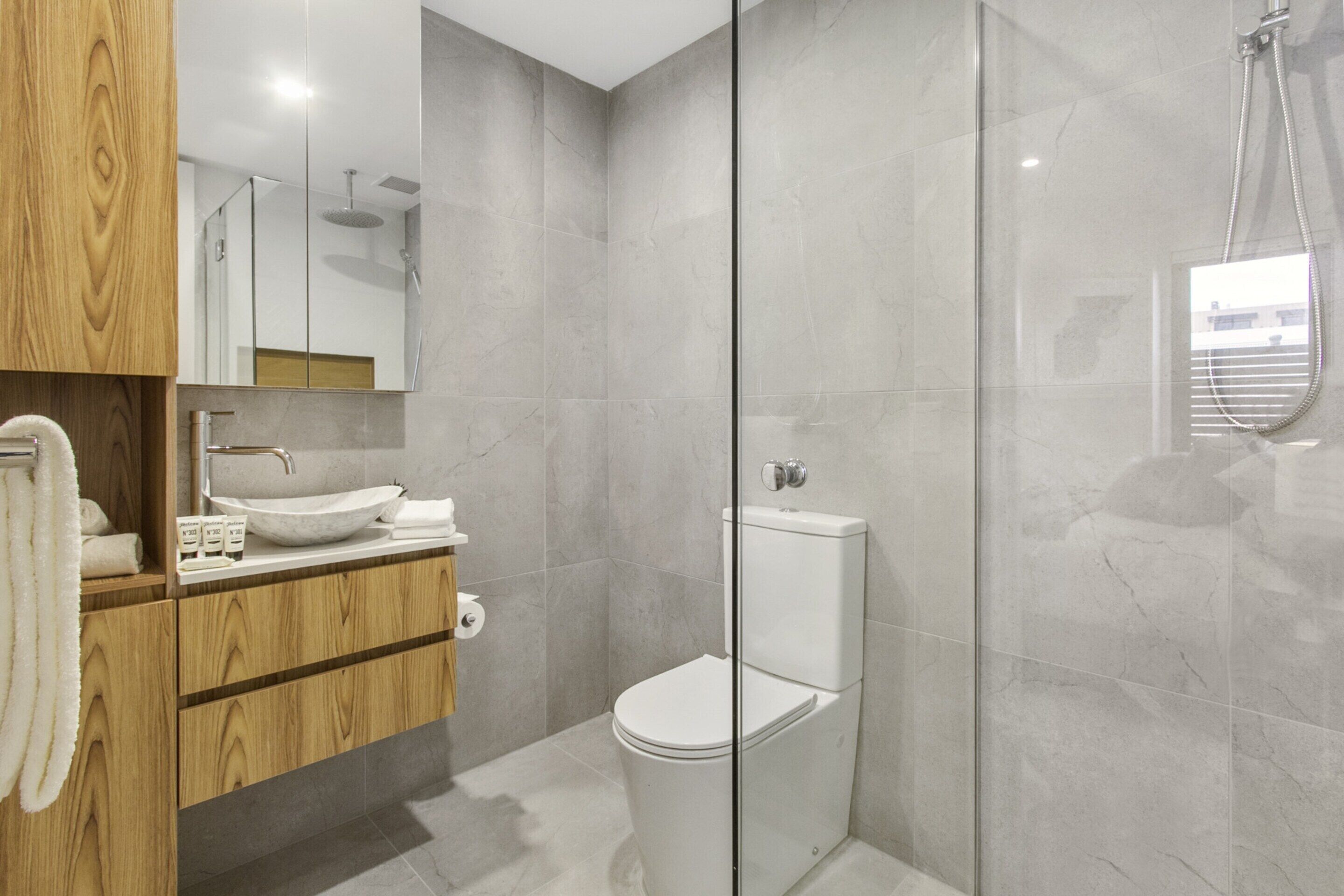 A modern bathroom with a wooden vanity, a white sink, and a glass-enclosed shower area.