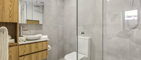 A modern bathroom with a wooden vanity, a white sink, and a glass-enclosed shower area.