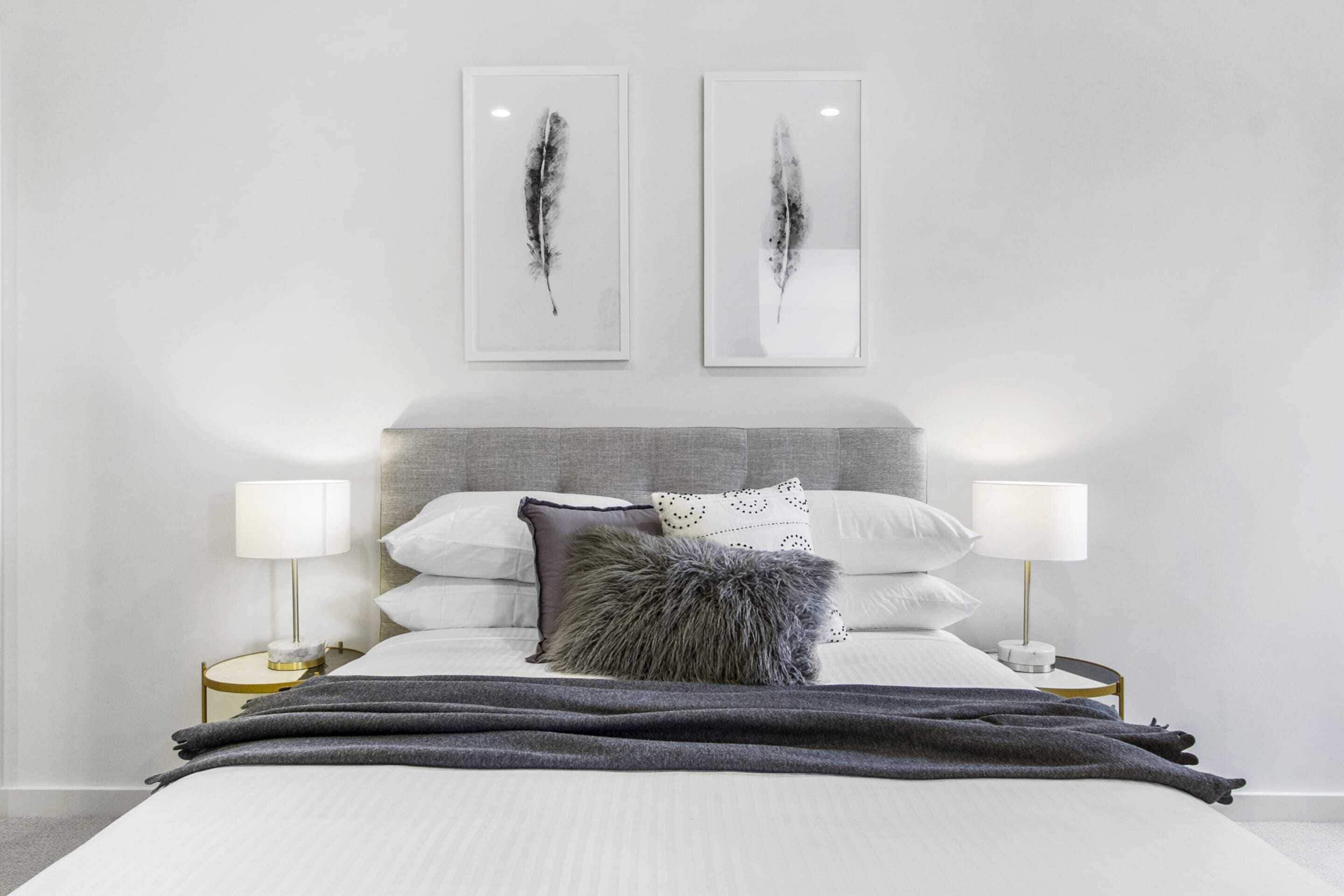 A neatly made bed with a grey headboard, white bedding, and two bedside lamps.