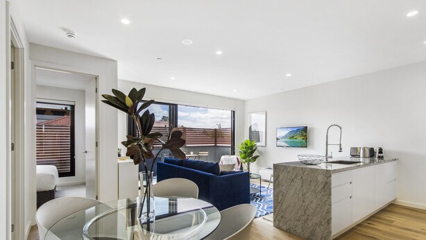 A modern kitchen with a marble countertop, a sink, and a dining area with a glass table and chairs. - Boutique Apartment in Quiet, Sought-after Suburb (Melbourne)