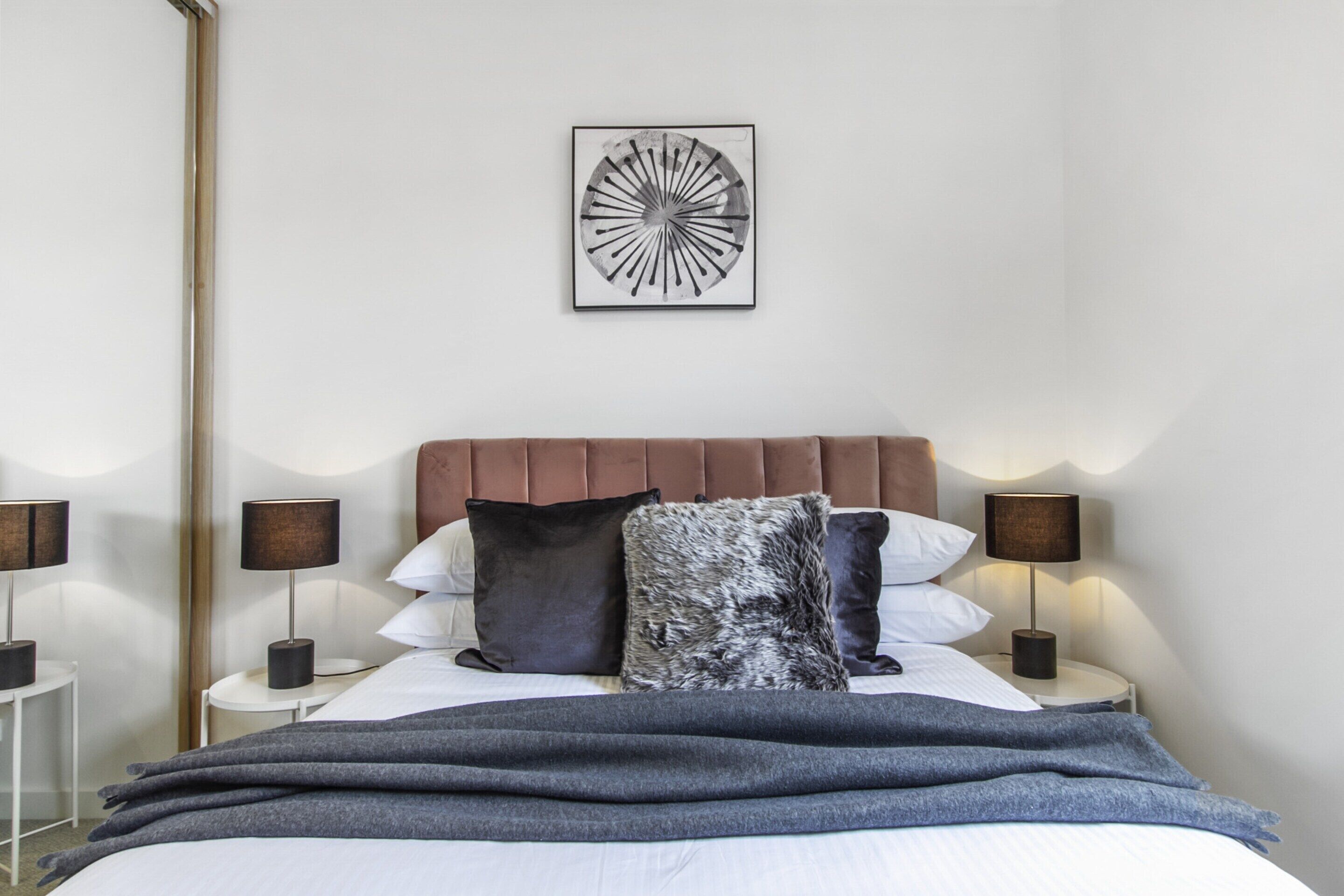 Een keurig opgemaakt slaapkamer met een groot bed, een hoofdbord, twee nachtkastjes en een kunstwerk aan de muur.